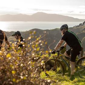 Four mountain bikers at the top of the Red Tape Track on Whareroa Farm, overlooking Kāpiti Coast and Kapiti Island.