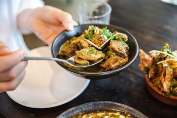 A person is spooning a portion of food from a dish at Chaat Street, a tapas-style Indian restaurant in Te Aro, Wellington.