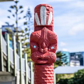 A traditional red Māori pou (carved post) with Wellington city in the background.