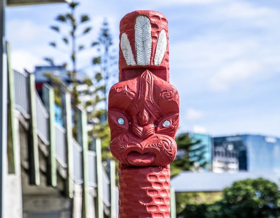 A traditional red Māori pou (carved post) with Wellington city in the background.