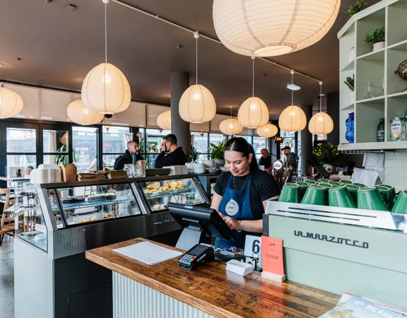 Modern café interior with hanging pendant lights, a glass food cabinet and a service counter in central Wellington.