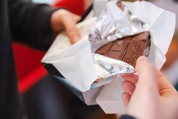 Two hands unwrap a bar of chocolate.