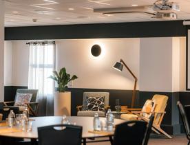 Lobby of Atura hotel. Blurry dining table in foreground and couches with lamp in background.