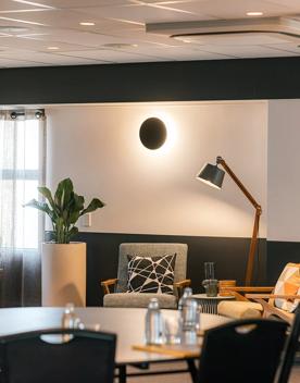 Lobby of Atura hotel. Blurry dining table in foreground and couches with lamp in background.