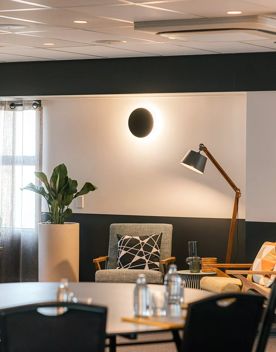 Lobby of Atura hotel. Blurry dining table in foreground and couches with lamp in background.