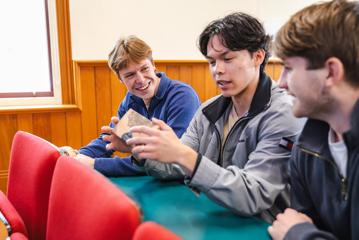 Three students sit next to one another in a lecture hall talking.