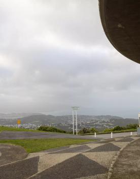 The Brooklyn Wind Turbine sits on a hill above Wellington, with views of the city. Bush and trees surround the area.