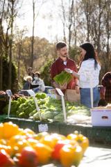 Two people picking up lettuce at an outdoor farmer's market.