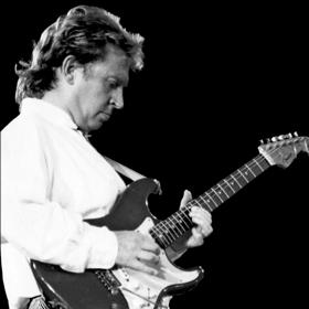 Andy Summers, the guitarist from The Police, plays the guitar in a white buttoned shirt.