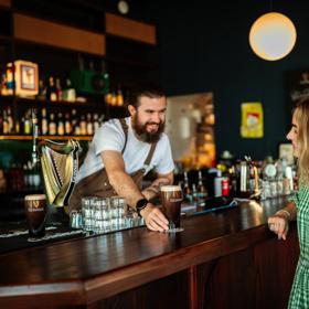 A smiling bartender passes a perfectly poured pint of Guinness to a happy patron at Regent cocktail pub.