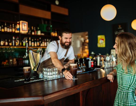 A smiling bartender passes a perfectly poured pint of Guinness to a happy patron at Regent cocktail pub.