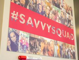 A photo board of the team at Strictly Savvy with the hashtag "savvysquad" written over it posted on the wall  at the company's office.