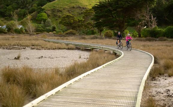 Wooden boardwalk crossing through an estuary with two people on bikes