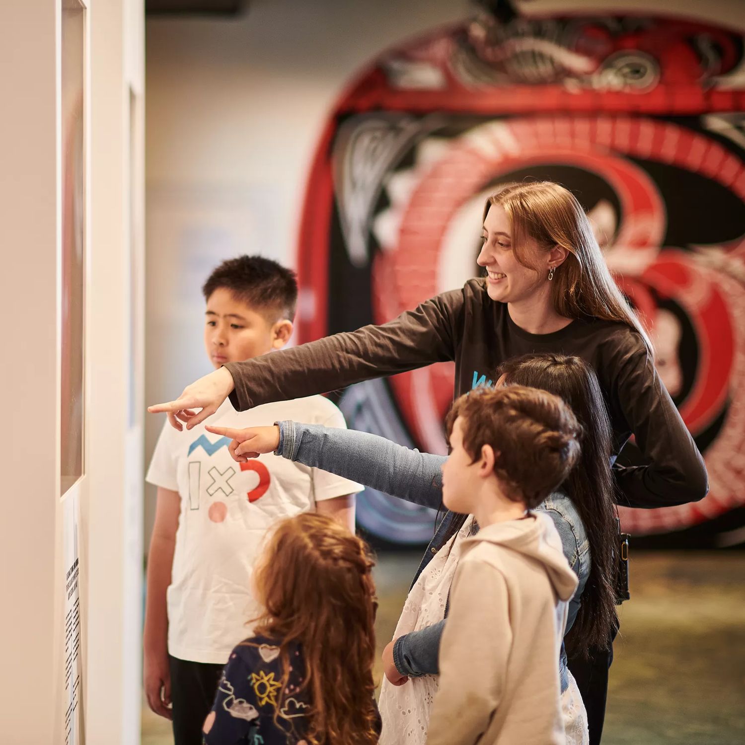 Four children and a tour guide look at a piece at the Te Whanganui-a-Tara exhibition at the Wellington Museum.