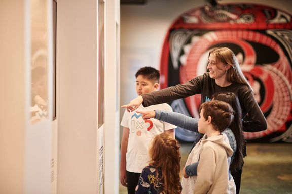Four children and a tour guide look at a piece at the Te Whanganui-a-Tara exhibition at the Wellington Museum.