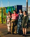 Four friends in colourful outfits standing in front of the Wellington sign on the Wellington waterfront in NZ.