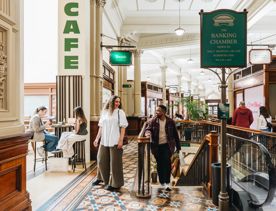 Two people walking up stairs inside the grand Old Bank Arcade.