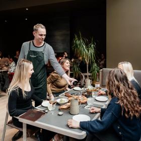 bartender pouring a glass of red wine to 4 customers sitting down and enjoying their food and drinks inside the Runholder.