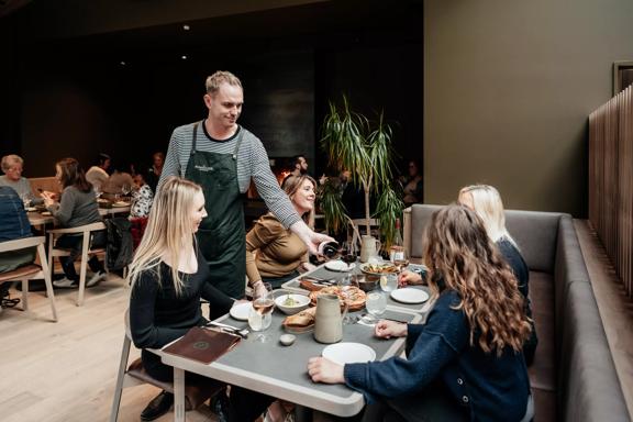 bartender pouring a glass of red wine to 4 customers sitting down and enjoying their food and drinks inside the Runholder.