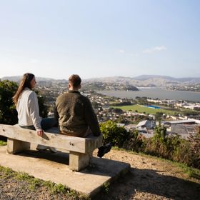 Two people sit on a bench at Rangitoto Lookout.