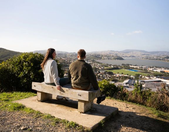Two people sit on a bench at Rangitoto Lookout.