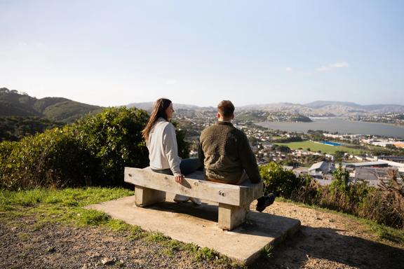 Two people sit on a bench at Rangitoto Lookout.
