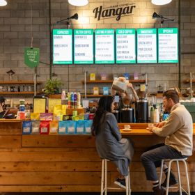 Two people sit at a counter drinking coffee at The Hanger café.