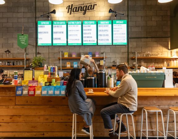 Two people sit at a counter drinking coffee at The Hanger café.