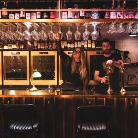 Two bar staff pour drinks at Puffin Wine Bar in dim lighting.