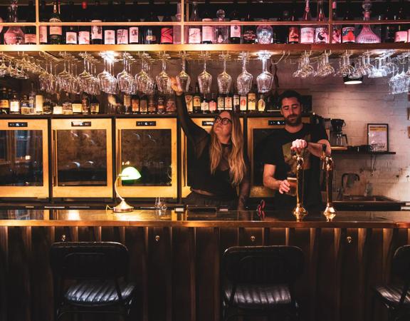 Two bar staff pour drinks at Puffin Wine Bar in dim lighting.