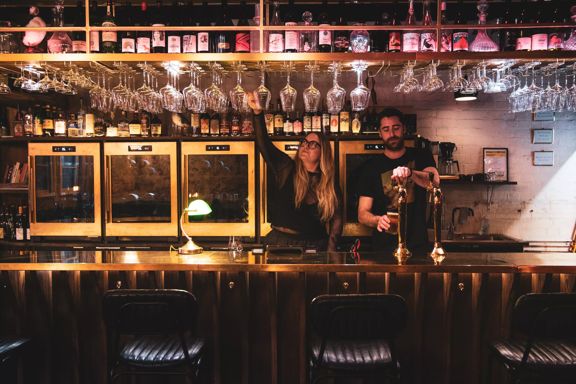 Two bar staff pour drinks at Puffin Wine Bar in dim lighting.