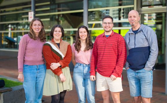 Five people stand in a row outside an office building.