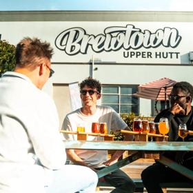 Three people drinking beer in front of Brewtown sign in Upper Hutt.