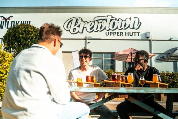 Three people drinking beer in front of Brewtown sign in Upper Hutt.