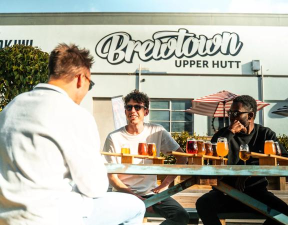 Three people drinking beer in front of Brewtown sign in Upper Hutt.