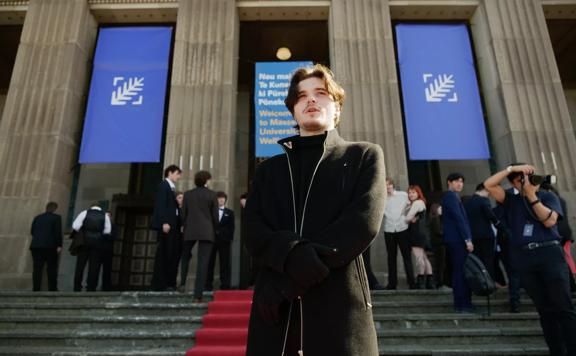 Flynn Biara Allen wears all black standing on the red carpet outside of the New Zealand Youth Film Festival. 