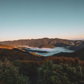 The sun rises over Remutaka Hill causing shadows on the forest. Mist sits in the valley.