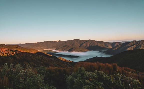 The sun rises over Remutaka Hill causing shadows on the forest. Mist sits in the valley.