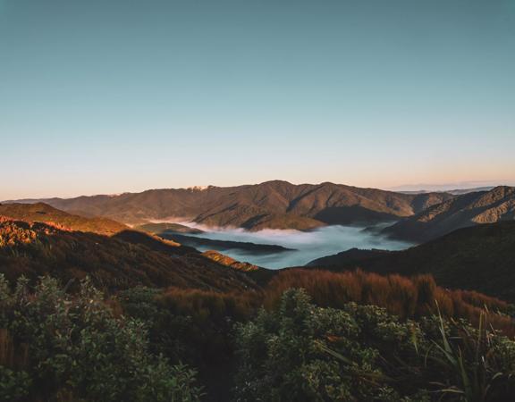 The sun rises over Remutaka Hill causing shadows on the forest. Mist sits in the valley.