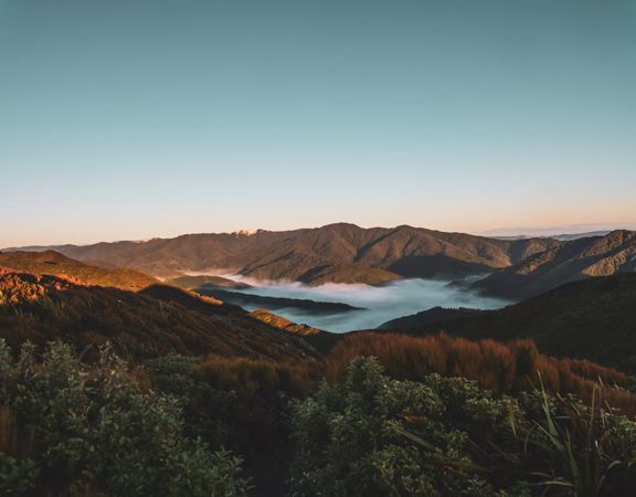 The sun rises over Remutaka Hill causing shadows on the forest. Mist sits in the valley.
