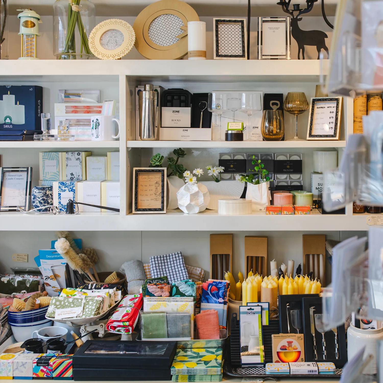 Various items sit on white shelves at Magnolia. From picture frames, to candles, to tea towels and glasses.