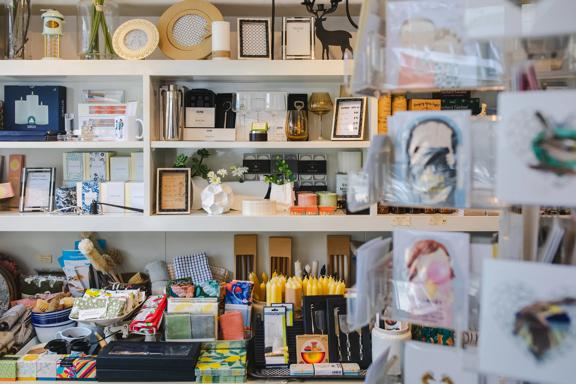 Various items sit on white shelves at Magnolia. From picture frames, to candles, to tea towels and glasses.