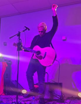 Musician Shayne P. Carter performing in a small, purple-lit room.