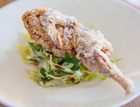 A leg of crispy Mutton bird sits on top of a green salad on a white plate.