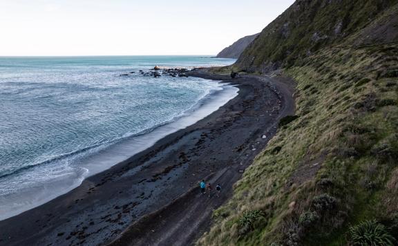 An aerial shot of three people walking along the Red Rocks Coast Walkway.