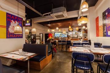 The inside of The Old Quarter, a Vietnamese restaurant on Dixon Street in Te Aro, Wellington. There are booths, tables and bar seating, a few colourful posters light the white walls and wicker lamps hang from the ceiling.