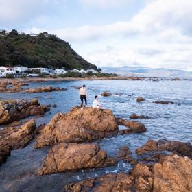 Two people on a rocky coastline on the Southern Walkway, a hiking trail in Wellington, New Zealand.