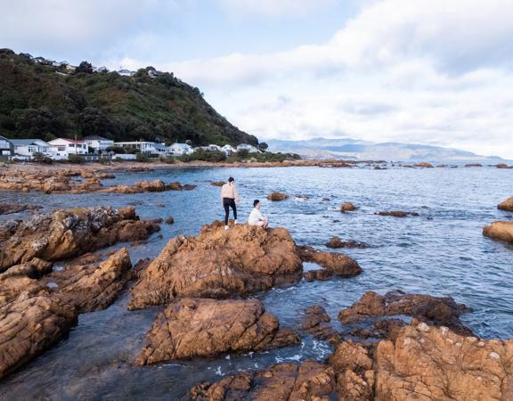 Two people on a rocky coastline on the Southern Walkway, a hiking trail in Wellington, New Zealand.