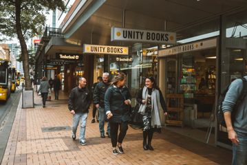 A group of people walk along Willis Street, with Unity Books store behind them and the signs above them.