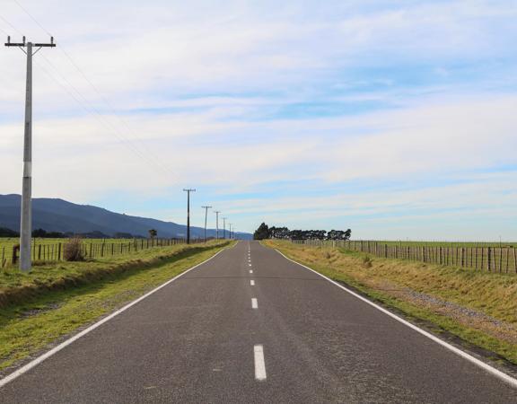 The rural Western Lake road, which connects the Remutaka Range to Lake Wairarapa, features lush green fields and mountains.
